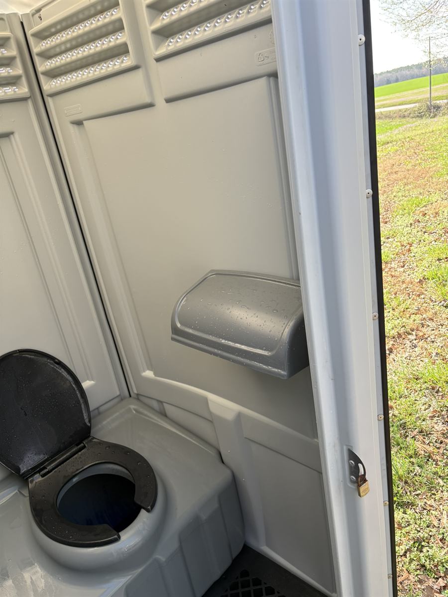 Open porta-john door showing clean interior on a job site